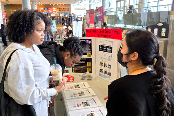 Two people talking to person at International Development at Humber info table
