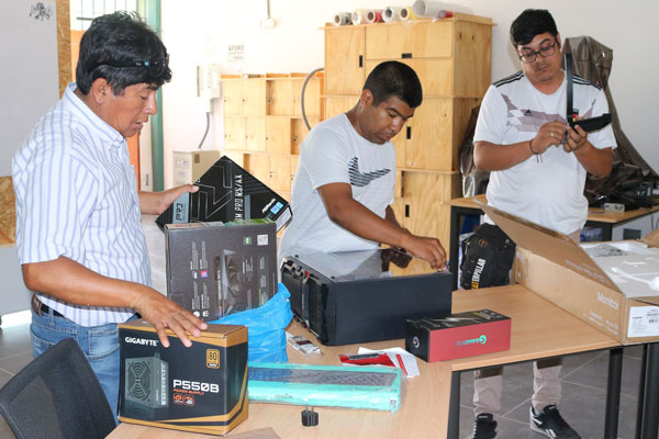 Three people standing around table looking at computer and tech parts